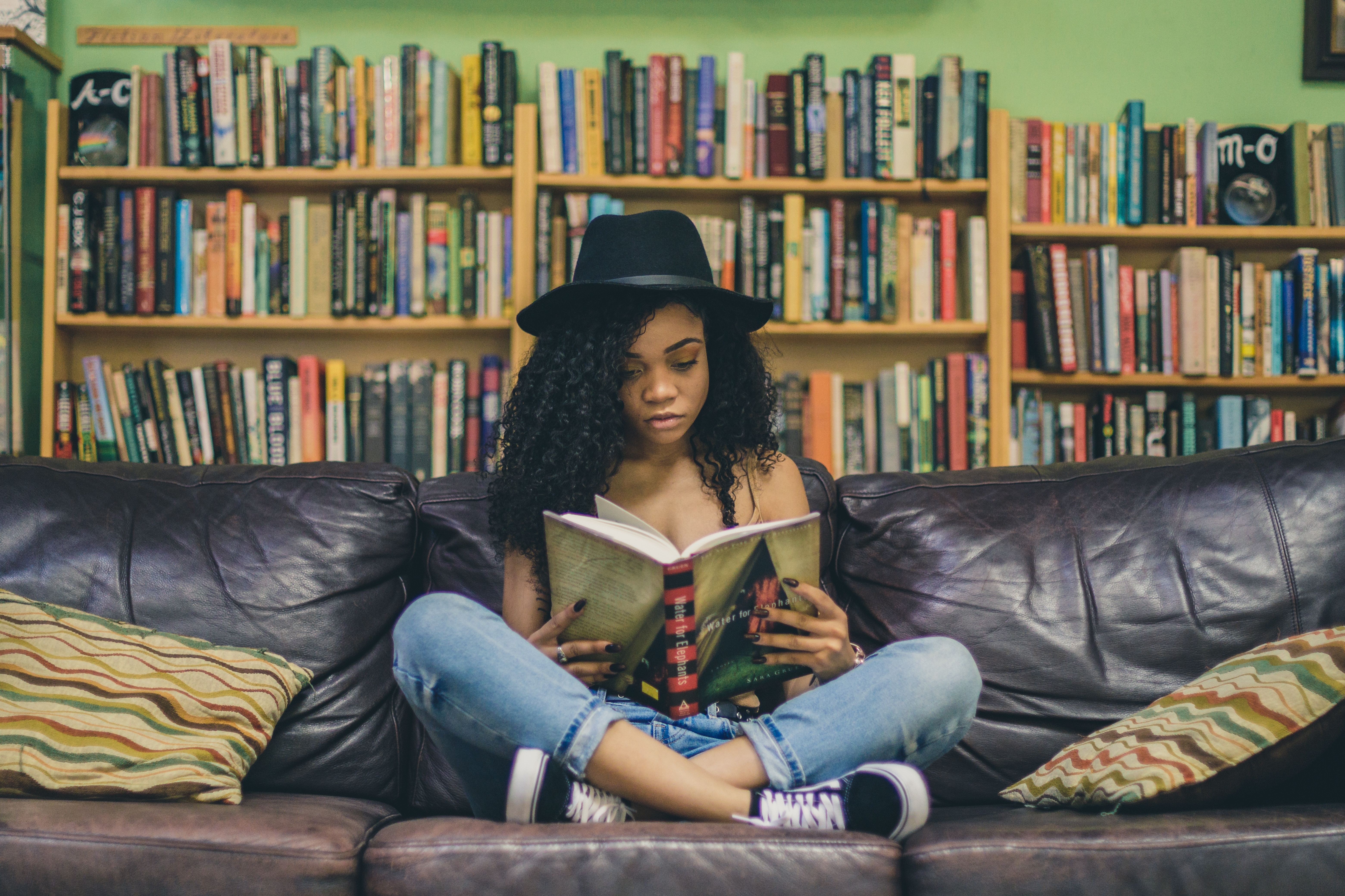 girl sitting on a couch in front of bookshelves reading "Water for Elephants"