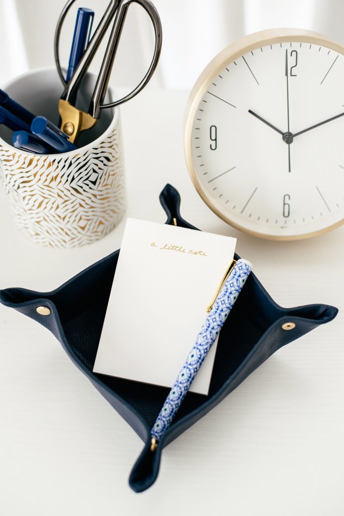 notebook and pen with a clock and cup of desk supplies