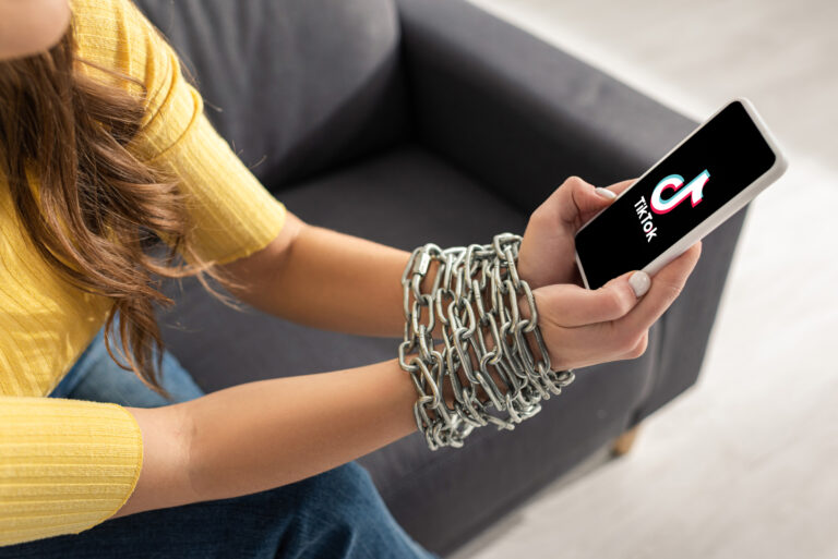 woman's hands chained while holding a phone with the open tiktok app
