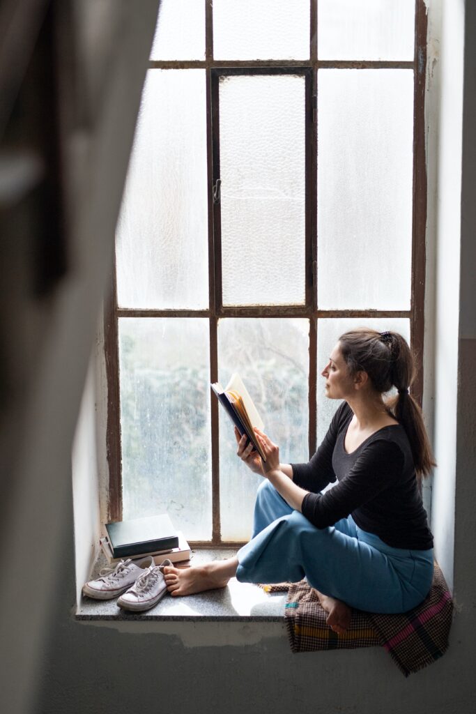 brunette woman sitting in a window seat reading a book