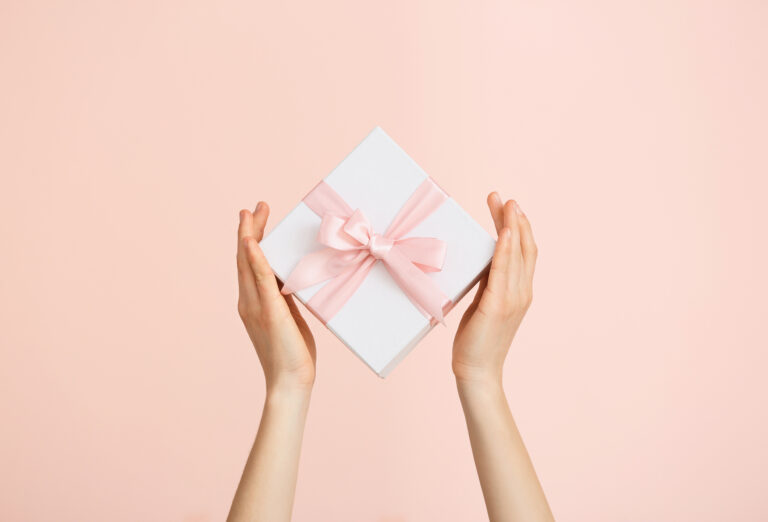 Female hands with beautiful gift box on color background