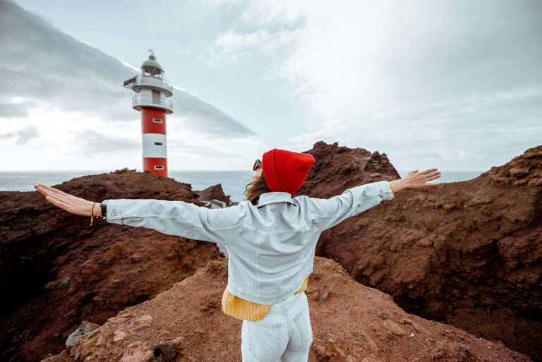 After the storm quotes - woman stands on hills by a lighthouse with arms widespread. Skies in the distance are darkly clouded