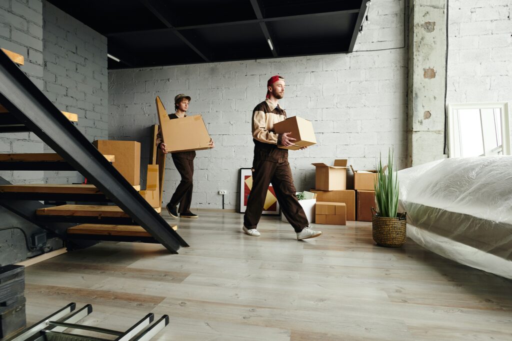 Two men carrying moving boxes across and apartment