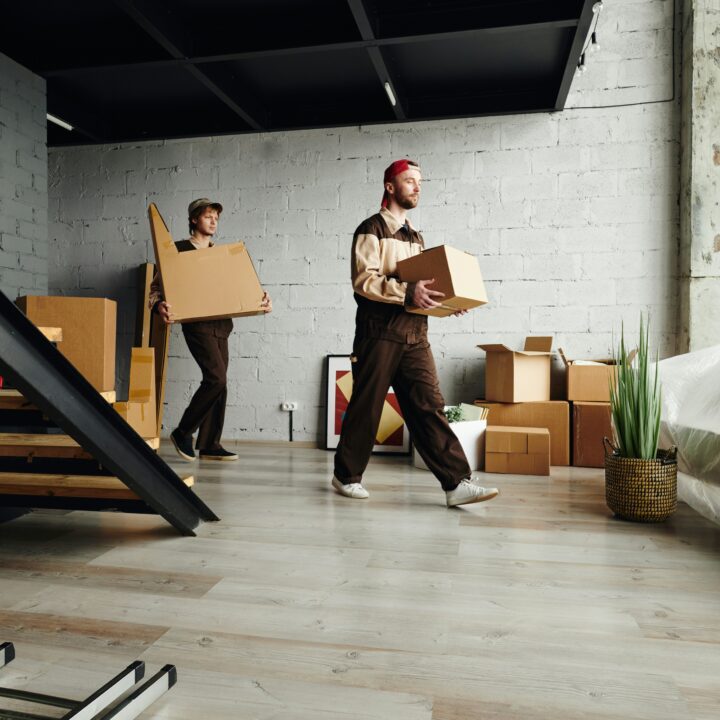 Two men carrying moving boxes across and apartment