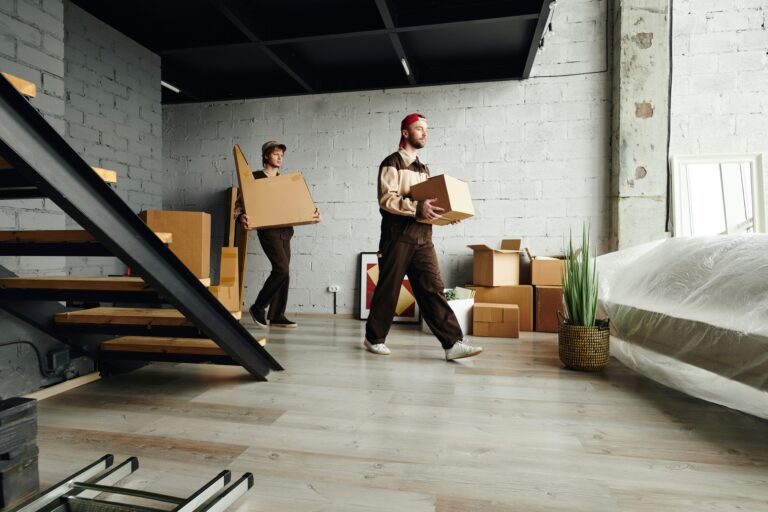 Two men carrying moving boxes across and apartment