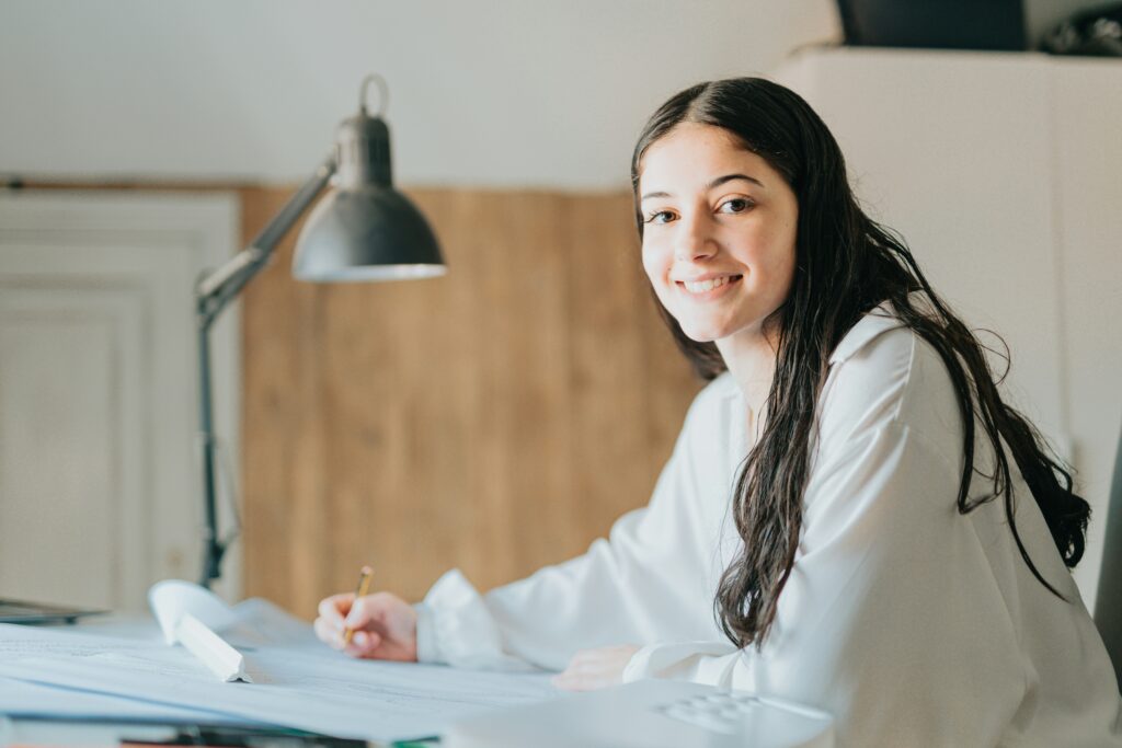 a young woman looks at the camera while working at a desk covered in papers