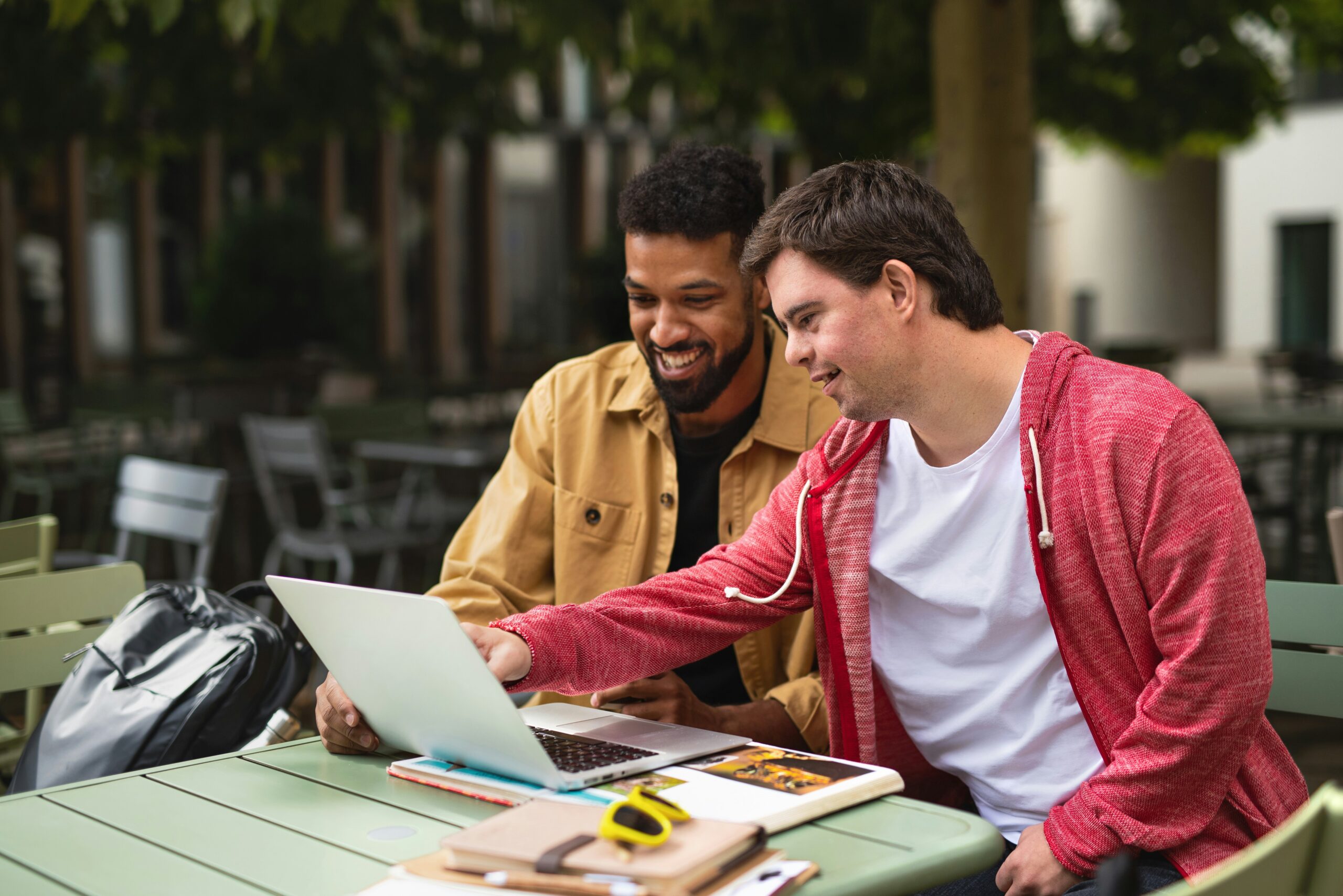 two guys are sitting together outside looking at a laptop