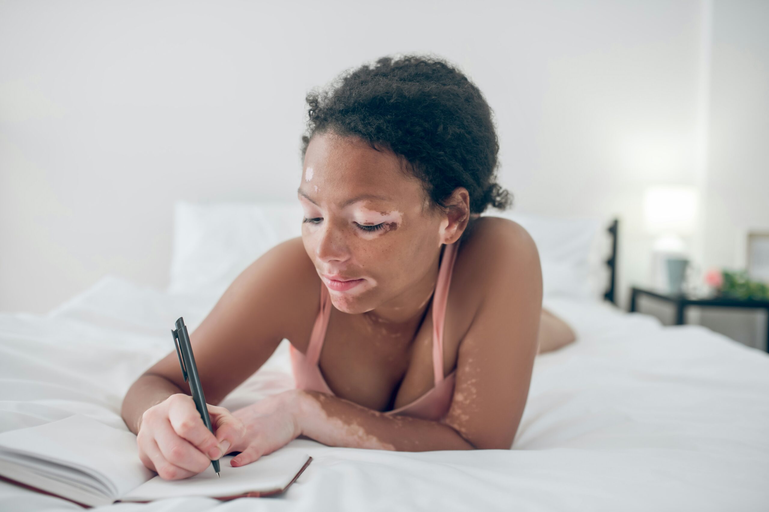 a young woman on her bed writes in a notebook in the morning