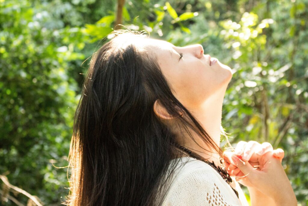 young woman with her eyes closed stands outside with her face lifted up to the sky and the sun is hitting her face
