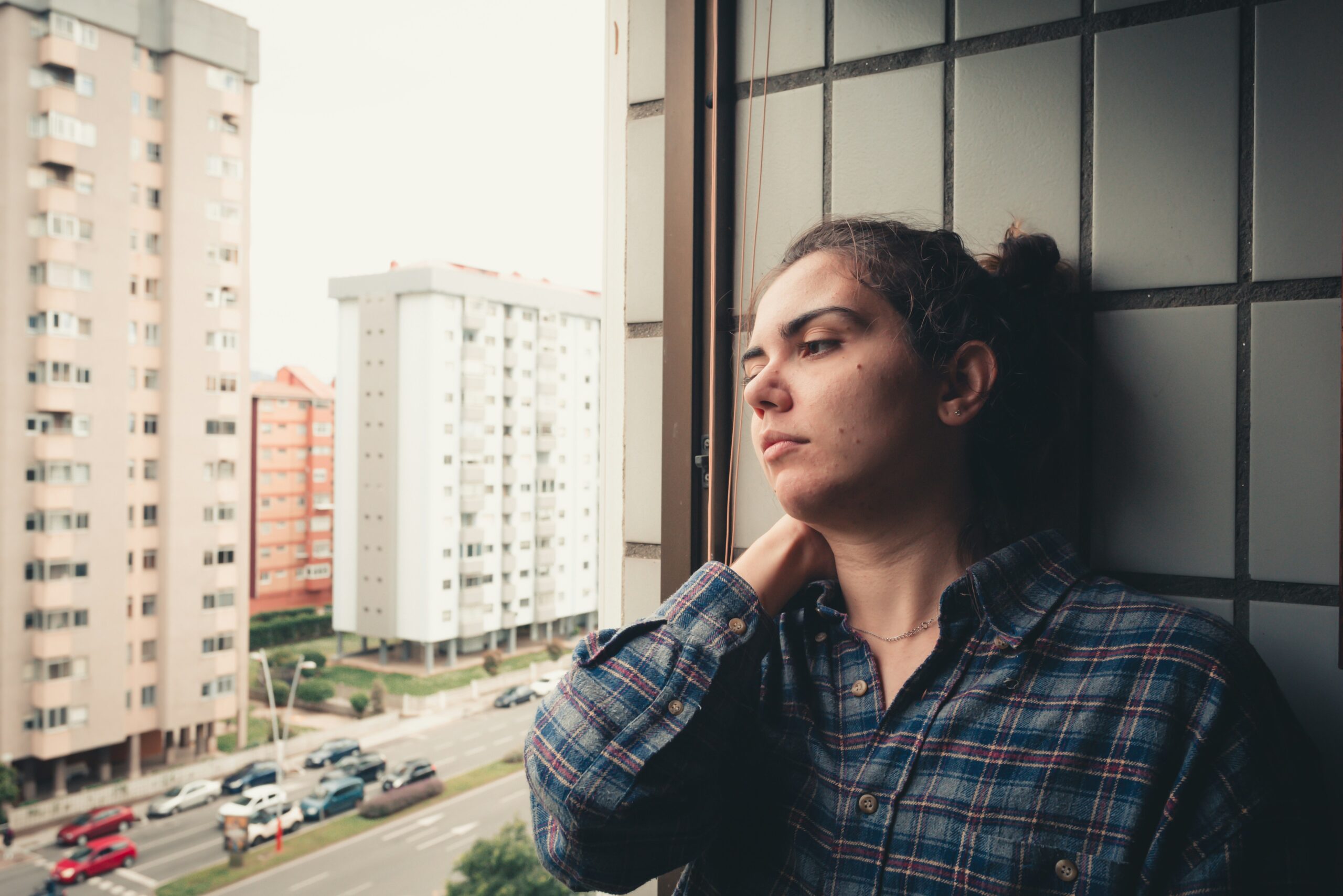 a young woman looks out a window in a city