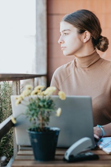 stoic young woman sits outside on a porch with her laptop