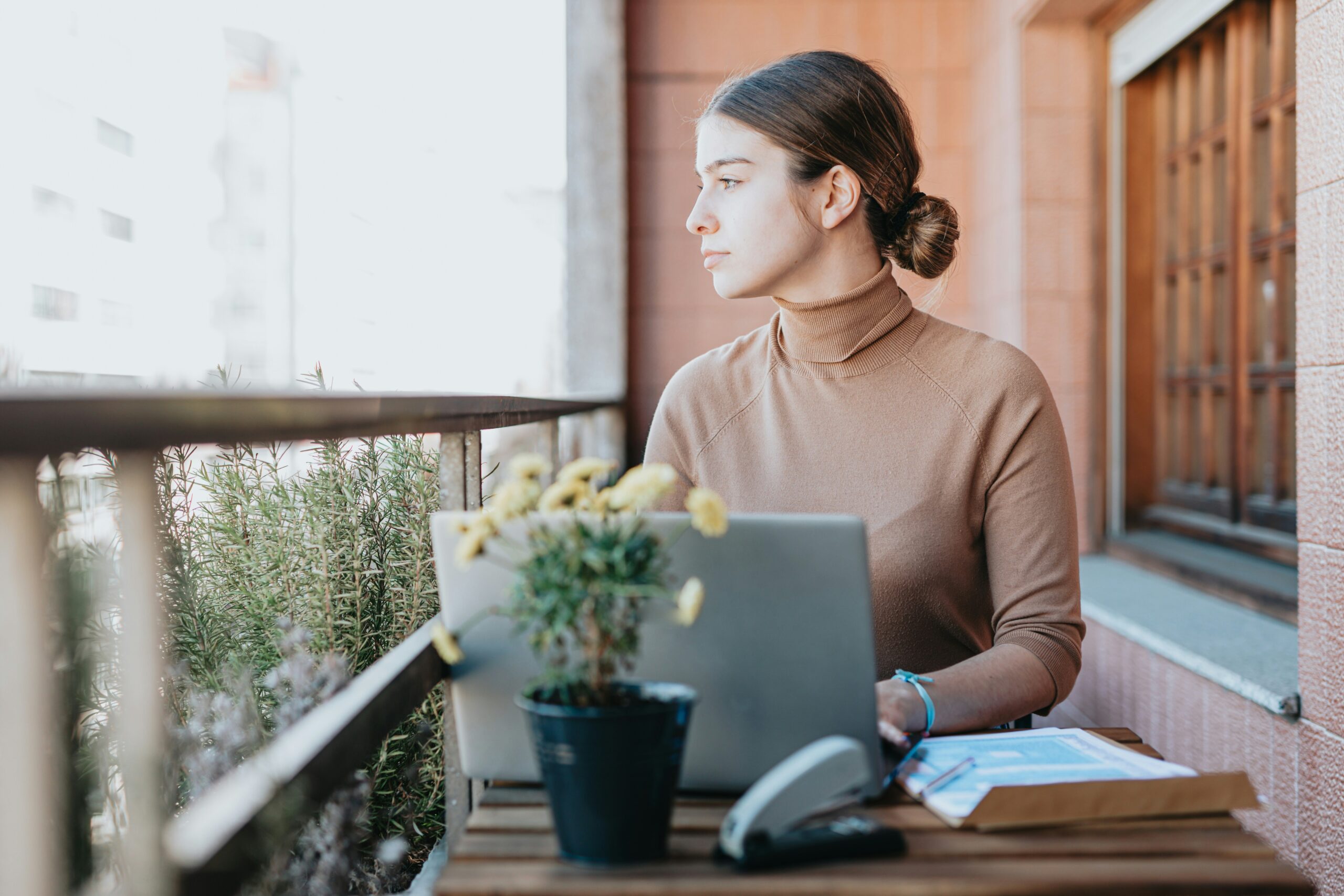 stoic young woman sits outside on a porch with her laptop