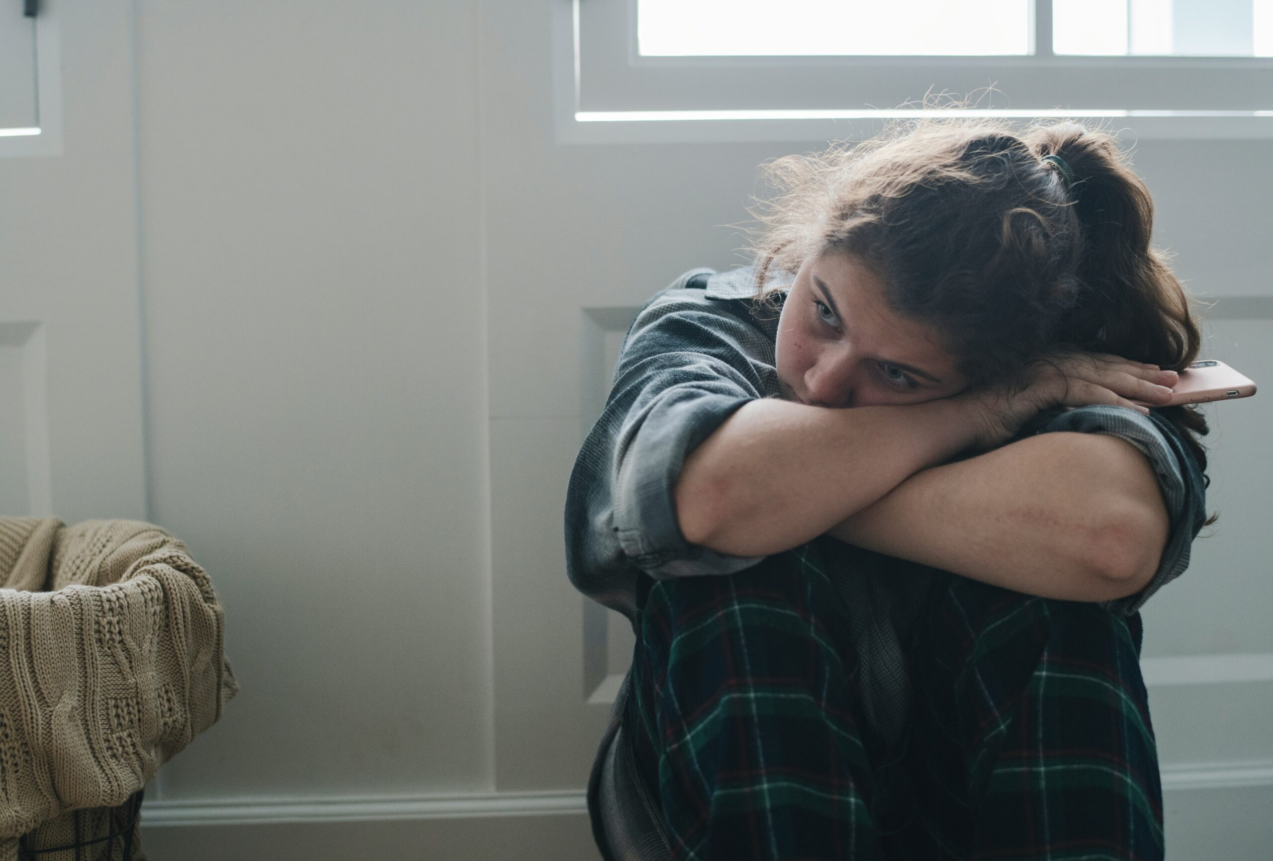 young woman sits alone looking sad and unkempt
